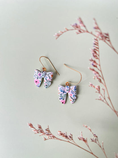 Bow shaped floral earrings on a light background with dried branches.