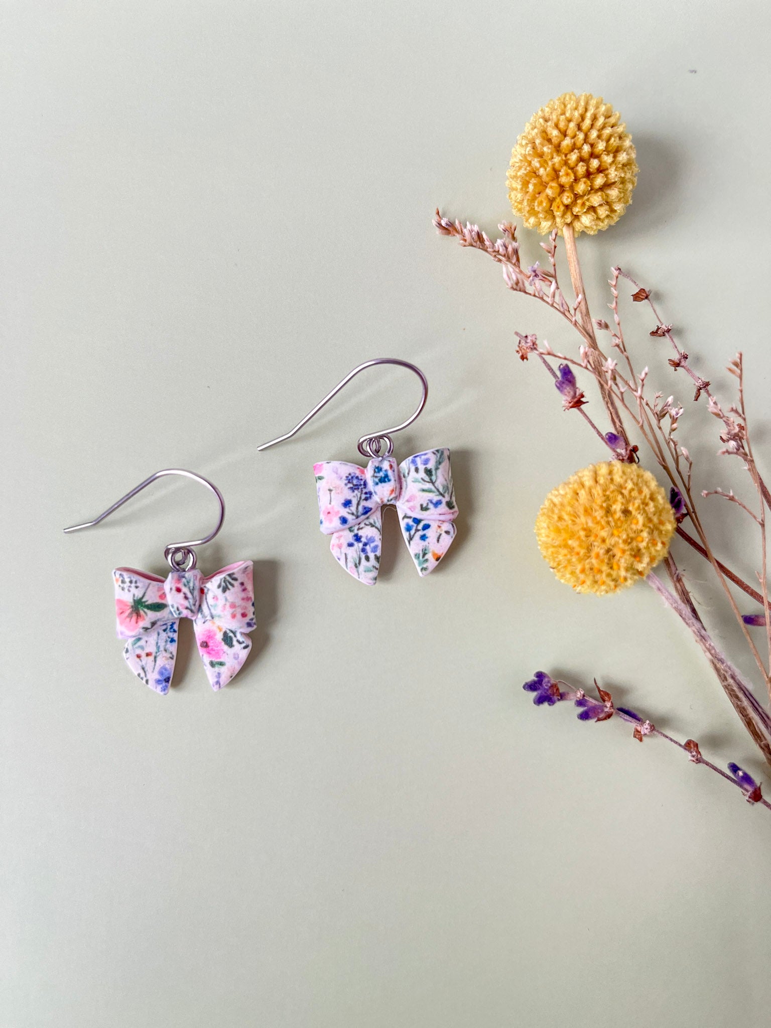 Floral earrings with a decorative yellow pom-pom on a light gray background