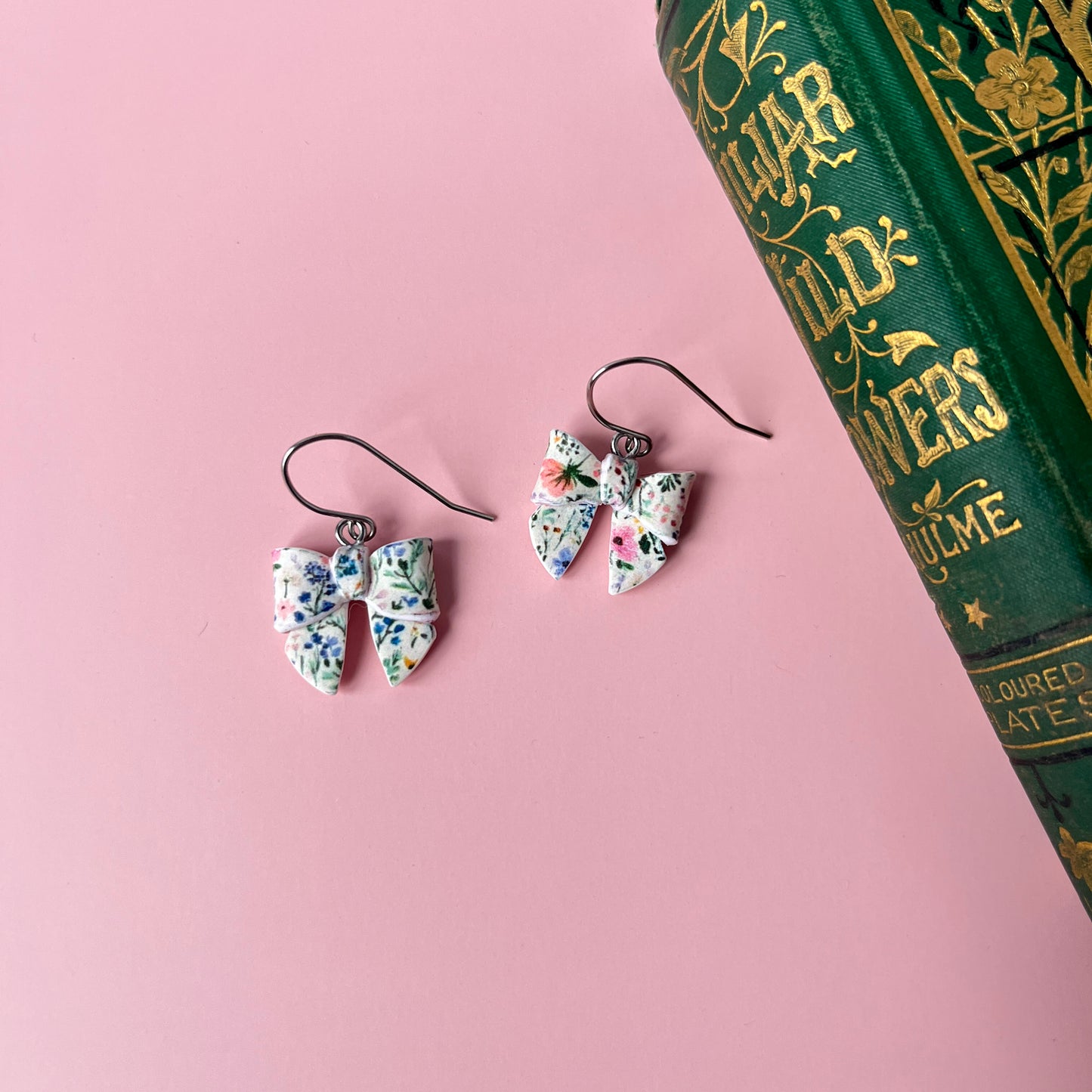 Floral earrings on a pink surface with a book in the background