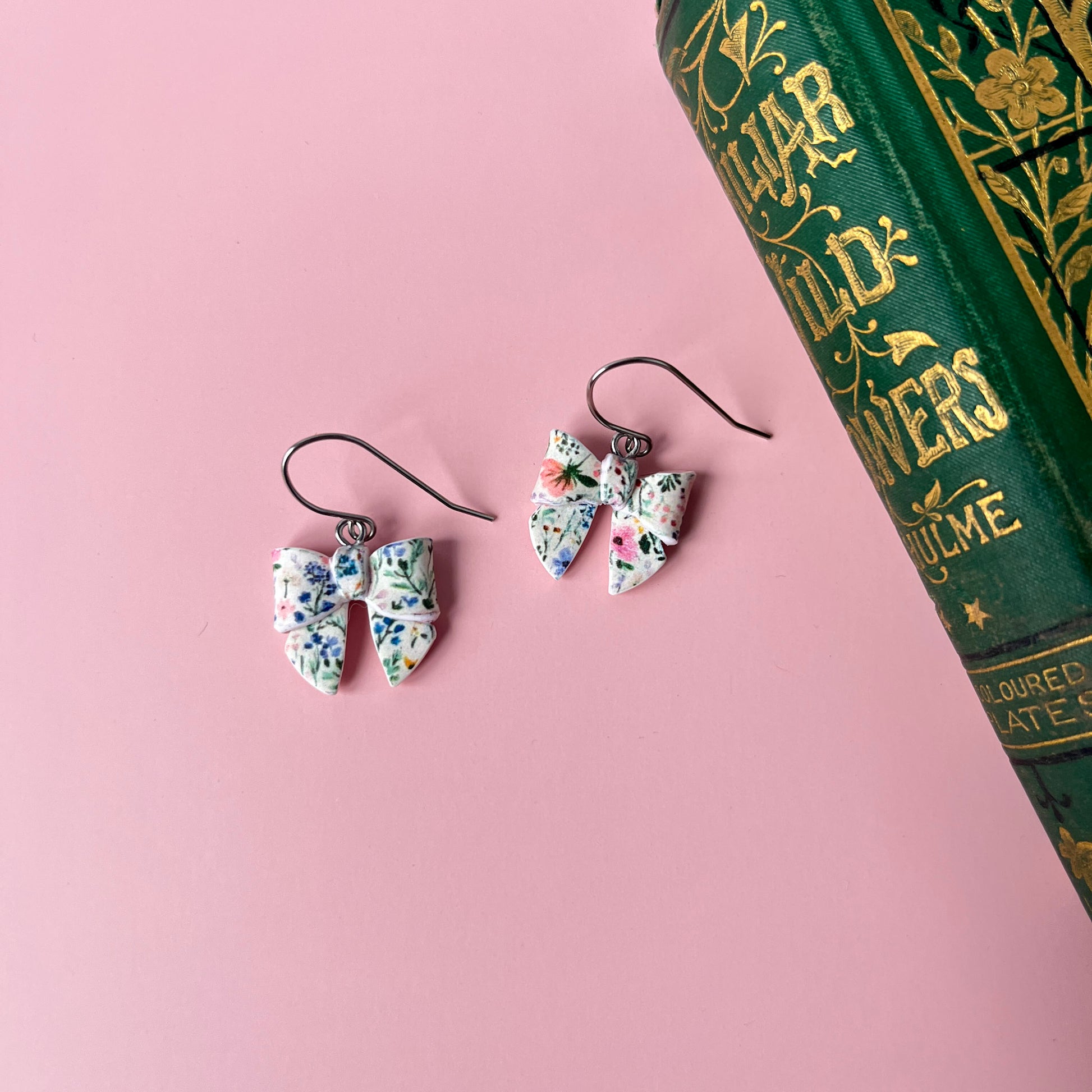 Floral earrings on a pink surface with a book in the background