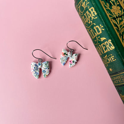 Floral earrings on a pink surface with a book in the background