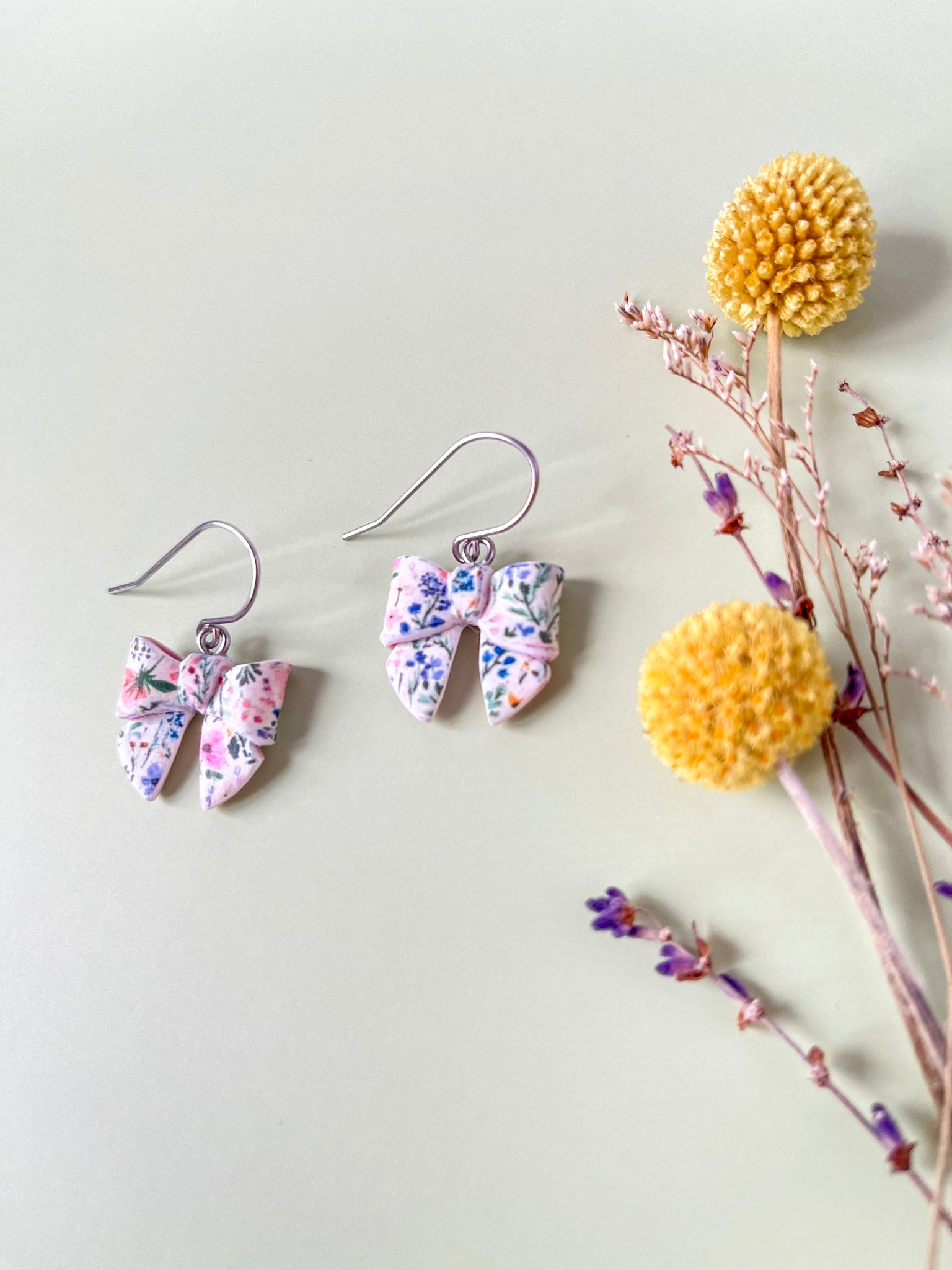 Floral-patterned bow earrings on a light surface with decorative elements.