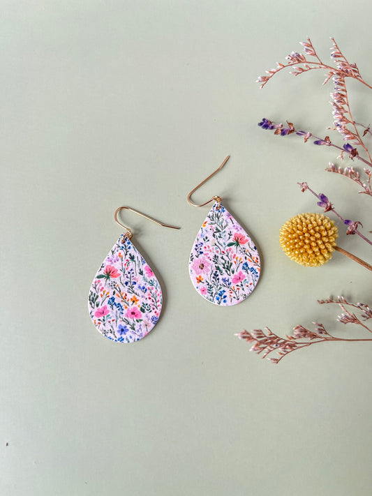 Teardrop-shaped floral earrings on a light gray background with dried flowers.